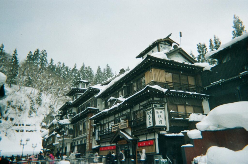 日本的溫泉及其特色 A picturesque view of traditional Japanese architecture in a snowy onsen town, set against a backdrop of snow-covered trees.