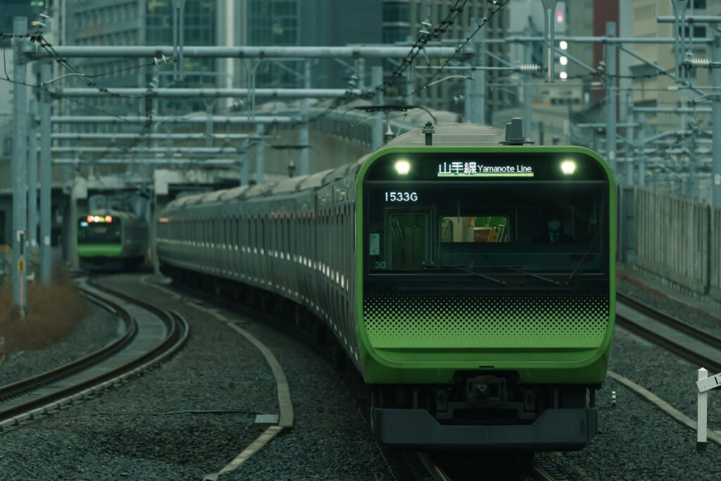 東京的JR山手線 a green train traveling down train tracks next to tall buildings