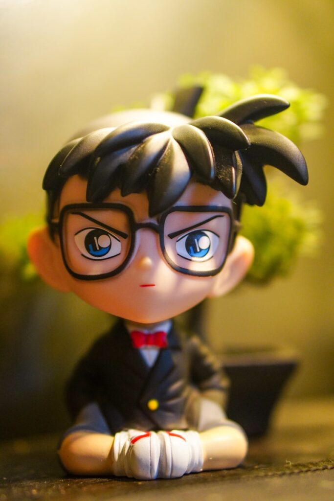 鳥取與柯南 a doll with glasses sitting on a table next to a potted plant